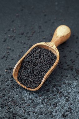 Koyu arkaplanda siyah susam tohumlarıyla dolu ahşap kepçe