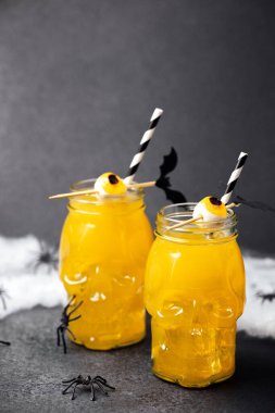 Kafatası kavanozlarında ürkütücü Cadılar Bayramı içkileri, ürkütücü gözler ve karanlık arka planda örümcekler.