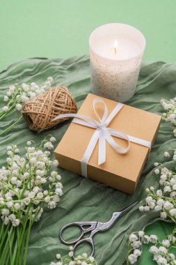 Yeşil kumaş arka planında hediye kutusu olan sicim, mum ve çiçekler.