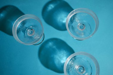 Berrak sıvıyla üç temiz bardak ve gölgeli mavi bir yüzey üzerinde kabarcıklar..