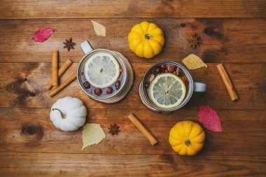 Limonlu ve dutlu sıcak içecekler, tarçın çubukları, balkabakları ve ahşap masadaki sonbahar yaprakları..