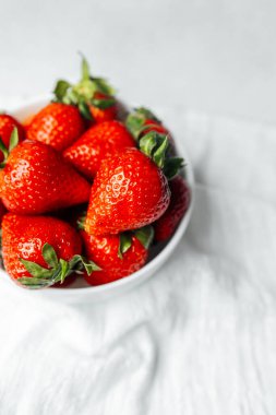 Sulu çilekler temiz bir yüzeyde beyaz bir kasede düzenlenir..
