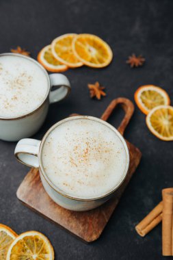 Sıcak köpüklü içecek, baharatla kaplanmış, seramik bardakta servis edilmiş, kurutulmuş portakal dilimleri ve tarçın çubuklarıyla.