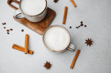 Tarçın çubuklu iki fincan kremalı latte ve açık gri arka planda yıldız anason.