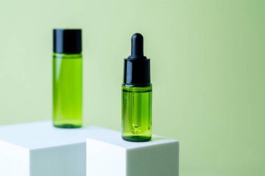 Siyah kapaklı yeşil kozmetik atık şişesi beyaz küp kaide arka planında eşleşen konteynır sergileniyor