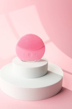 Pembe yuvarlak silikon yüz temizleme cihazı beyaz silindirde duruyor.