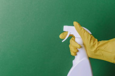 Sarı eldiven, yeşil arka planda temizlik için sprey şişesi.