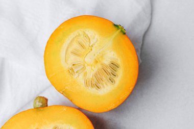 Portakal kabağı ikiye bölünmüş yumuşak beyaz kumaş arka planda tohumları ve eti gösteriyor..