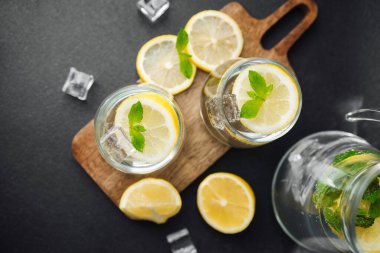 Taze nane yapraklı turunçgil limonatası ve güneşli yaz mutfağında parlak bir masada cam sürahi içinde buz küpleri.