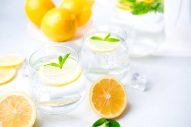  İki bardakla taze limonlar ve parlak masa üzerinde nane yapraklı ve buz küplü bir sürahi limon suyu.