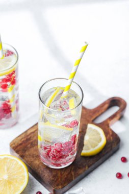 İki uzun bardakta limon kırmızısı üzümlü su ve ahşap tahtada buz küpleriyle pipet.