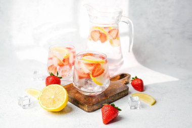 Sürahide çilekli limon ve buz küpleri ve taze meyvelerle servis edilen bardaklar.