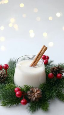 Çam çelengi ve kırmızı böğürtlenlerle çevrili tarçın çubuklu bir bardak kremalı kış içeceği..