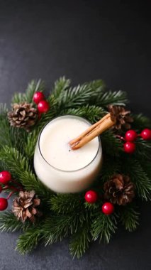 Çam dalları, böğürtlen ve koni ile çevrili, tarçın çubuklu kremalı kış içeceği.