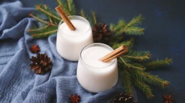 İki kremalı kış içeceği, üzerinde tarçın çubukları ve çam iğneleri olan mavi bir kumaş.