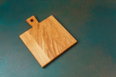 A wooden cutting board rests on a green surface, ideal for food preparation activities.