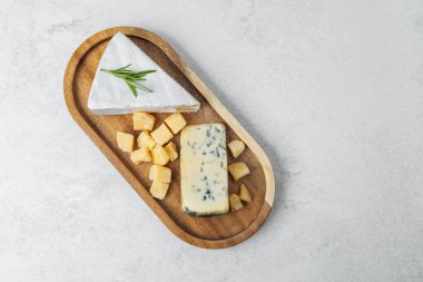 Farklı peynir türleri güzel bir şekilde ahşap bir tabakta otlarla sıralanmıştır..