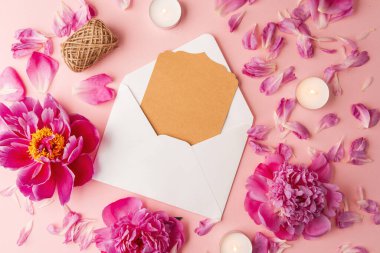 Üzerinde şakayık çiçekleri, taç yaprakları, mumlar ve pembe masanın üzerinde jüt sicimi olan tebrik kartı zarfı.