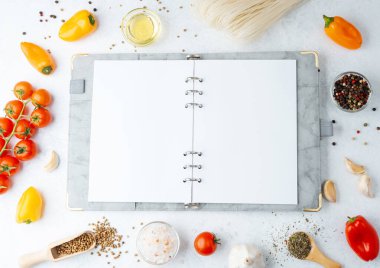 open cookbook with various cooking ingredients around on white background
