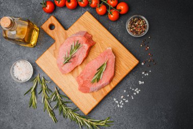 Kesme tahtasında biberiyeli çiğ biftek. Etrafı kiraz domatesleri, yağ tuzu ve biberle çevrili.