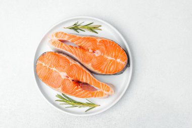 Fresh salmon fillets ready for cooking, garnished with rosemary on a white plate.