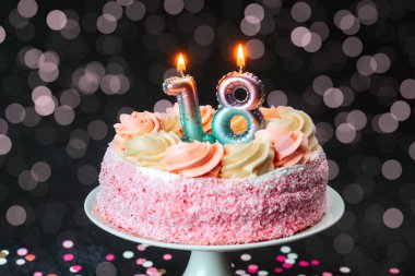 Dondurmalı, mumlu ve etrafa saçılmış renkli konfetiyle pembe bir doğum günü pastası..
