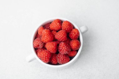 Organik gıda veya vegan diyet konsepti için hafif yüzeyde beyaz kasede ahududu.