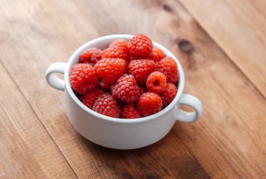 Beyaz kasede ahududu. Kırsal gıda tasarımı ya da organik yeme konsepti için ahşap masa üzerinde