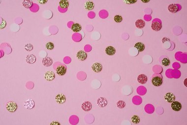 Bright confetti in various colors spread across a pink surface, perfect for festivities.