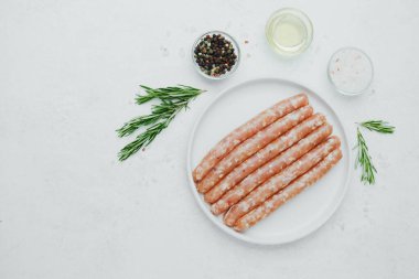 Biberiye ve baharatlı, beyaz tabakta pişmemiş sosisler.