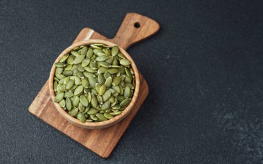 Balkabağı tohumları tahta kasede kesme tahtasının üzerinde siyah arka planda