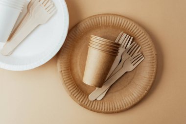 Brown and white disposable paper cups and wooden forks on beige background