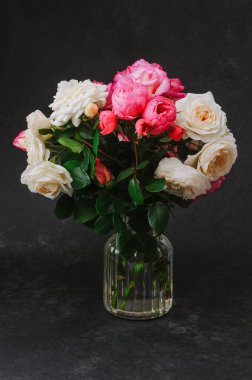 White and pink roses in a clear glass vase with dark textured background