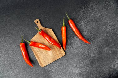 Kırmızı biberler sanatsal olarak bir mutfaktaki tahta kesme tahtasına yerleştirilir..