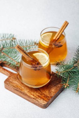 Warm drinks with lemon slices, star anise, and cinnamon sticks on a wooden board, fir branches