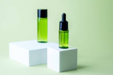 Siyah kapaklı yeşil kozmetik atık şişesi beyaz küp kaide arka planında eşleşen konteynır sergileniyor