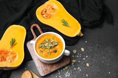 Butternut squash soup topped with seeds and rosemary next to halved squash on dark surface