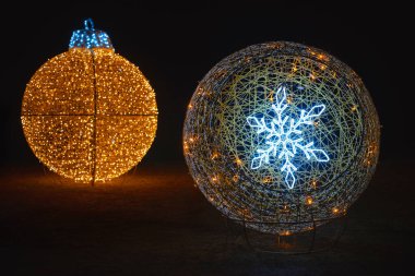 İki parıldayan şenlik süsü, bir altın top, bir kar tanesi küresi, gece.