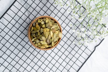 Karışık tohumlar süslü bir şekilde sade bir kasede, tel askıda çiçeklerle dizilir..