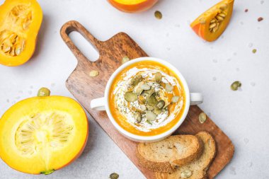 Kremalı balkabağı çorbası kasesi ve tahtanın üzerinde kızarmış ekmekle servis edilen tohumlar.