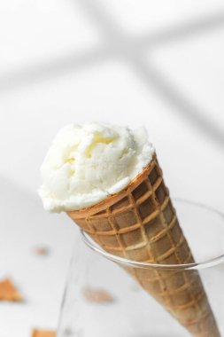 Kremalı vanilyalı dondurmalı waffle külahı parlak arka planda, kırıntıları olan berrak bardakta dinleniyor.