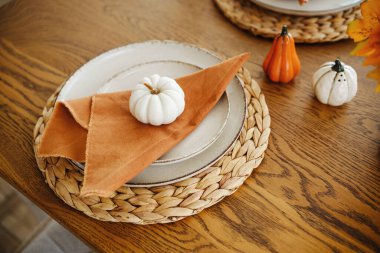 Autumn table setting with small pumpkins on plates, woven mats, and orange napkins.