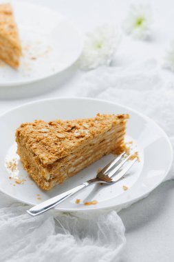Delicious Napoleon cake slice on white plate with fork. Layered pastry cream dessert.