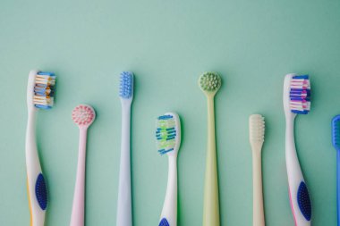 Various toothbrushes lined up on a clean pastel green background, oral hygiene tools arranged neatly.