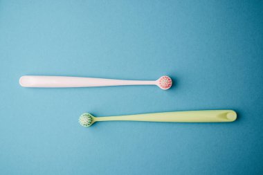 Two pastel colored tongue scrapers lay flat on a plain blue background.