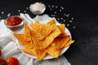 Domates soslu nachos tabağı ve siyah yüzeyde beyaz kumaşlı domatesler.