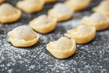 Siyah taş zemin üzerine un serpiştirilmiş taze pişmemiş cappelletti.