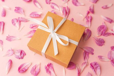 Dağınık şakayık yaprakları ve pembe gruplaşmış beyaz kurdeleli hediye kutusuna yakın çekim.