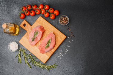 Kesme tahtasında biberiyeli çiğ biftek. Etrafı kiraz domatesleri, yağ tuzu ve biberle çevrili.