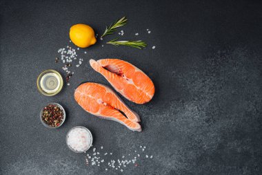 Somon filetoları koyu bir yüzeyde bitkilerle, limonla ve baharatlarla sıralanır..